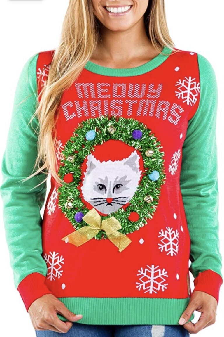 A woman rocks a wild “Meowy Christmas” sweater—green sleeves, red snowflake chaos, cat in blinged-out wreath and Santa hat. Purr-fect!.