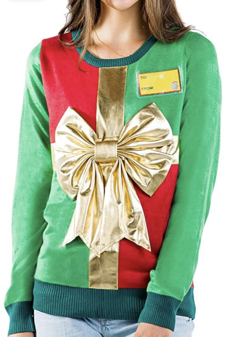 A woman rocks the Women’s Giant Gift Bow Sweater—green and red gift-wrap style, mega gold bow, flashy yellow tag. Festive chaos!.